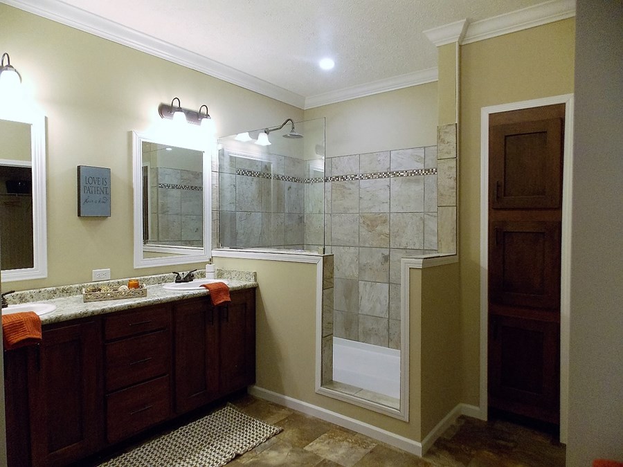 Cozy bathroom with tiled shower, brown vanity, and granite countertop. Soft lighting creates a warm ambiance. Wall art reads, "Love is Patient".