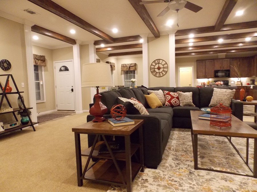 Cozy living room with a dark gray sectional sofa adorned with patterned pillows. A rustic coffee table and lamps add warmth under exposed wood beams.