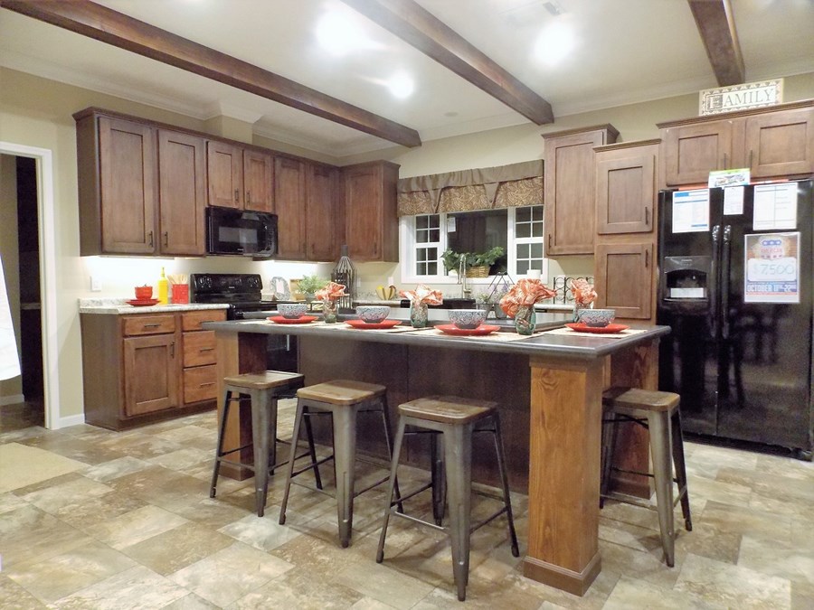 A cozy kitchen with wooden cabinets, stone-tile flooring, and a large island. Four stools surround the island, set for dinner with red plates and bowls.