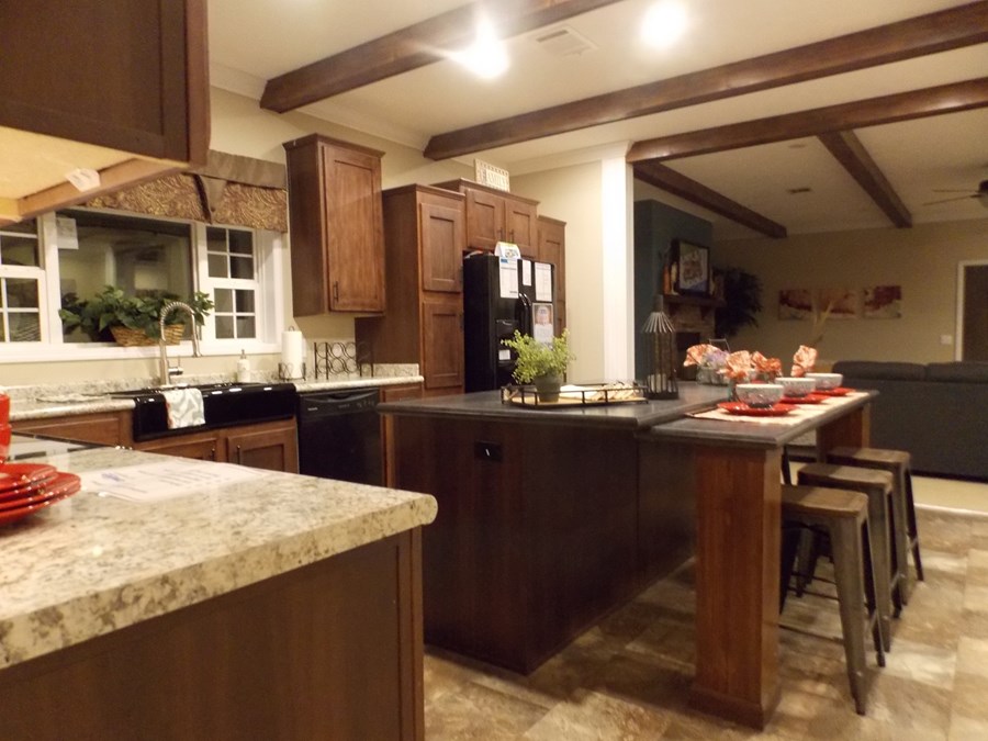 Warm, inviting kitchen with dark wood cabinets, stone countertops, and a large island. Bar stools and bright decor create a cozy, welcoming atmosphere.