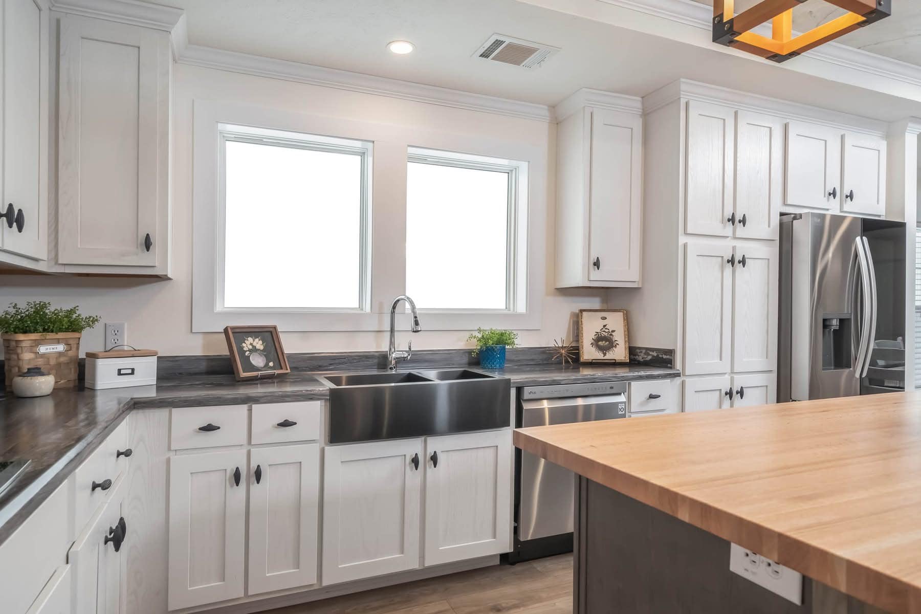Bright kitchen with white cabinets, a stainless steel farmhouse sink, and a wooden island. Windows provide natural light, creating a cozy, inviting atmosphere.