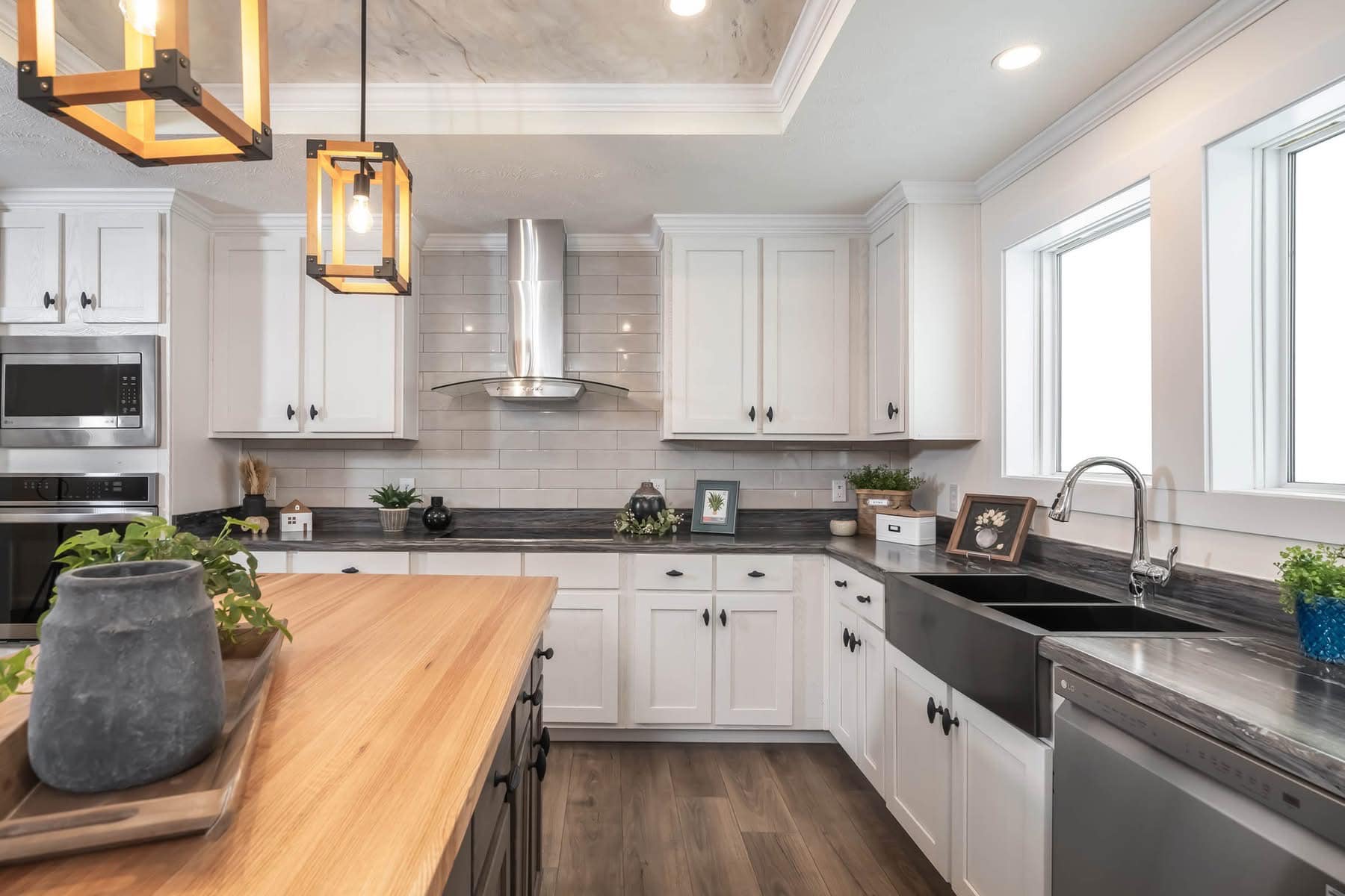 Spacious kitchen with white cabinets, stainless steel appliances, and dark countertops. Wooden island with plants and modern pendant lights overhead. Sleek and inviting atmosphere.