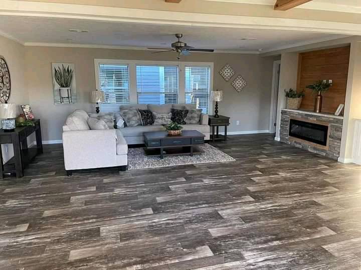 A spacious living room with a gray sectional sofa, coffee table, and modern decor. Large windows, hardwood floors, and a built-in fireplace create a cozy ambiance.