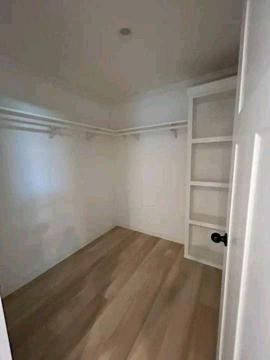 An empty walk-in closet with light wood flooring, white walls, and a ceiling light. It has shelves on the right and hanging rods on two walls.