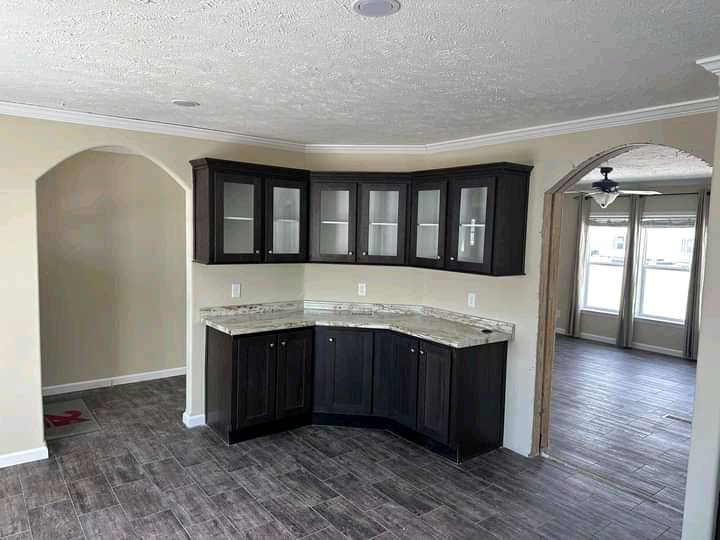 Modern kitchen corner with dark wood cabinets, glass doors, and marble countertop. Light beige walls, wood tile floor. Bright and inviting space.
