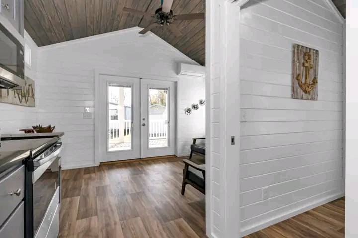 Bright, modern kitchen with wood flooring, white shiplap walls, and a wooden ceiling. Double French doors lead to a sunlit patio. Warm and inviting.