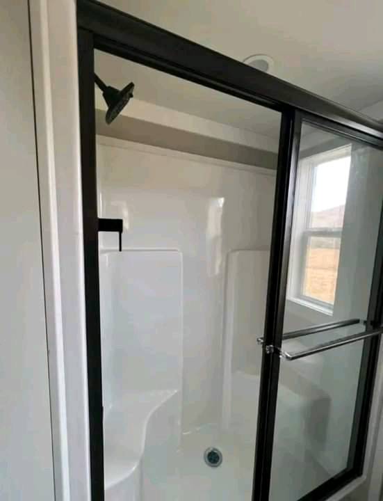 Modern bathroom shower with black-framed glass door, white interior, built-in bench, and overhead showerhead. Window allows natural light.