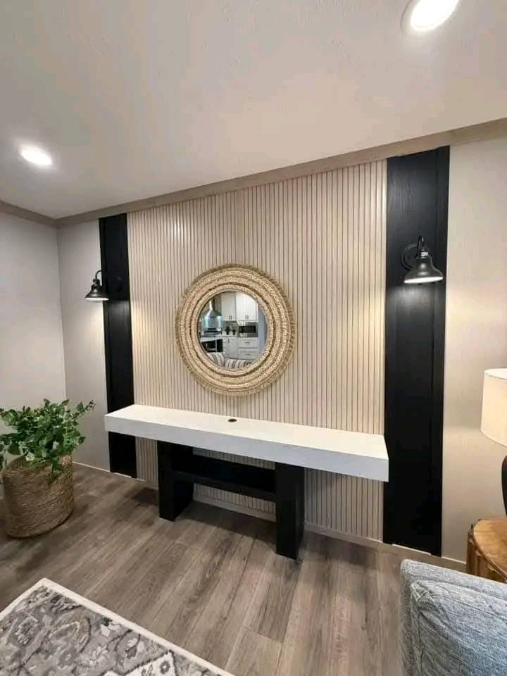 Modern living room with a decorative wood-panel wall featuring a round mirror. A sleek white console table stands below, flanked by wall-mounted lamps.