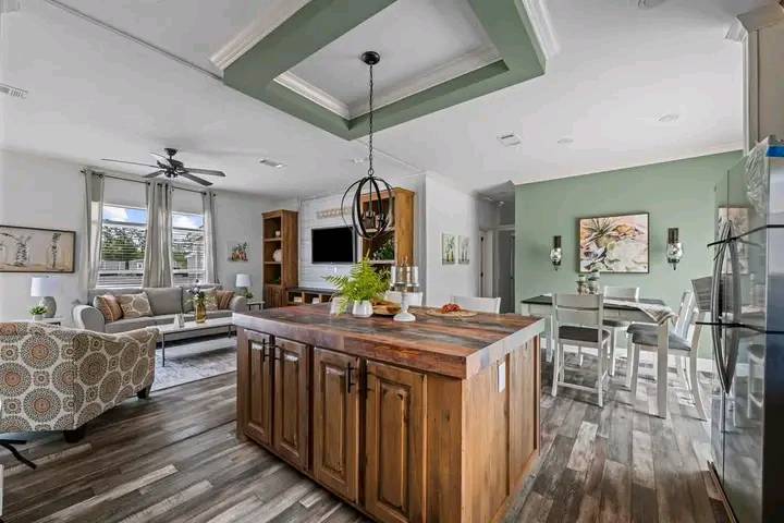 Spacious open-concept living area with a wooden kitchen island, a cozy lounge with a gray sofa, decorative armchair, and a dining table, exuding warmth.