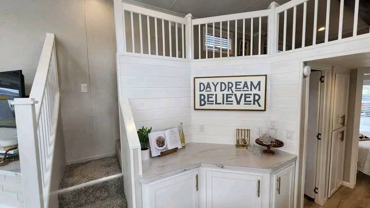 Cozy interior with white walls and a white staircase on the left. A framed "Daydream Believer" sign hangs above a marble counter with decor items.