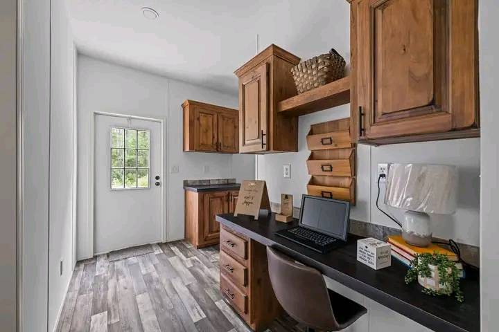 Cozy home office with a wooden desk and chair, brown cabinets, and a laptop. A door and window offer natural light, creating a warm, inviting space.