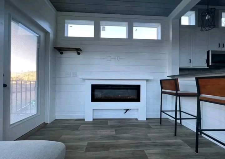 Cozy room with white shiplap walls, a modern electric fireplace, high windows, and a bar with wooden stools. The ambiance is bright and minimalist.