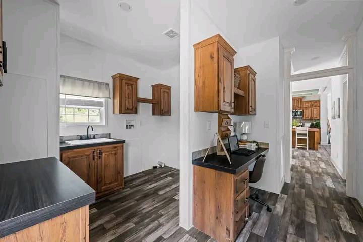 Spacious kitchen with light wood cabinets, dark countertops, and modern wood flooring. An adjacent desk area with a chair creates a cozy, functional space.