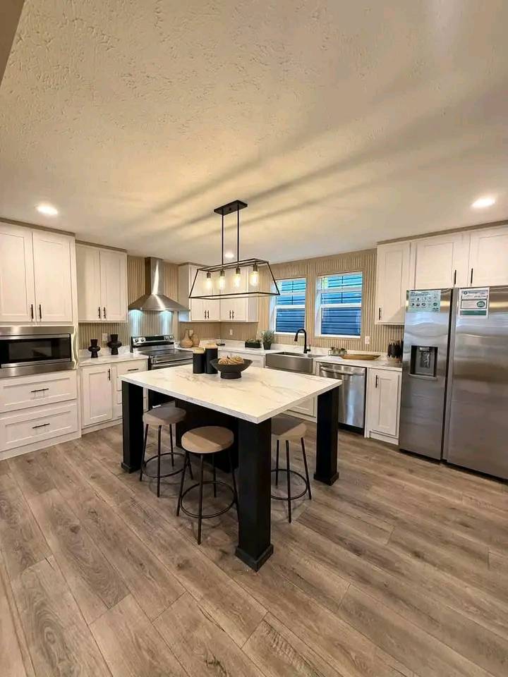 Spacious modern kitchen with white cabinets, stainless steel appliances, and a central island with bar stools. Wood flooring adds warmth and charm.