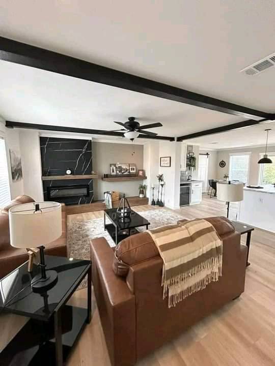 Modern living room with brown leather sofas, a black marble fireplace, and wooden beams on the ceiling. A cozy and elegant atmosphere is conveyed.