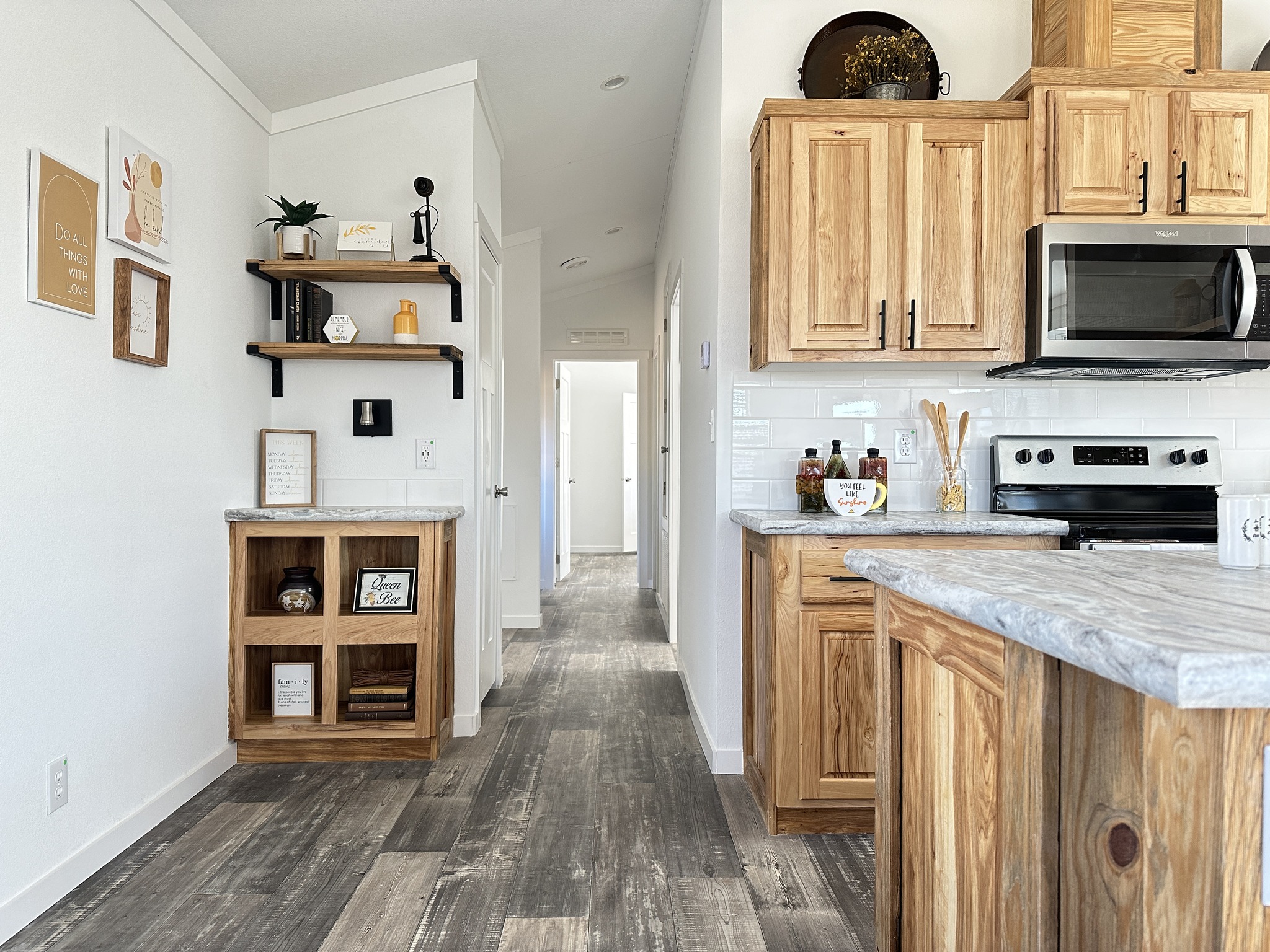 Modern kitchen with light wood cabinets, stainless steel appliances, and marble countertops. A narrow hallway leads to another room. Cozy and inviting.