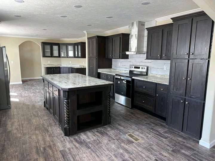 Spacious kitchen with dark wood cabinets, a large island with marble countertop, stainless steel appliances, and wood-patterned flooring.