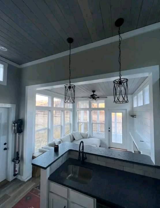 Bright room with large windows, a cozy white sectional, black countertop with sink, elegant pendant lighting, and a ceiling fan. Airy and modern feel.