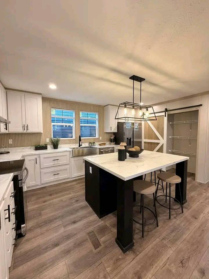Spacious kitchen with a central island, modern lighting, light wood floors, white cabinets, and a barn-style sliding pantry door. Cozy and inviting.