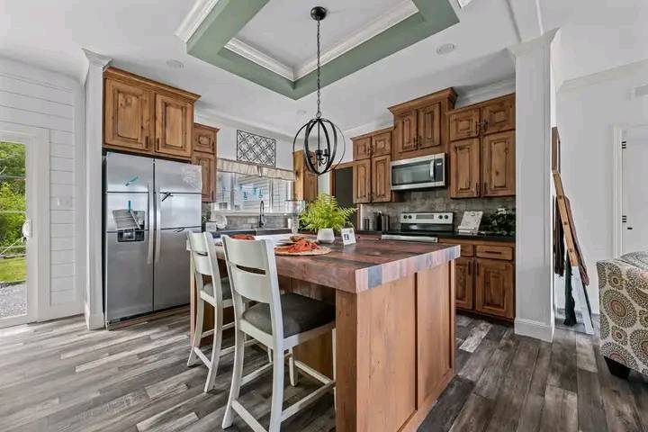 Modern kitchen with wooden cabinets and flooring, stainless steel appliances, and a central island with two chairs. Bright, airy, and inviting atmosphere.