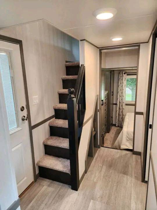 Compact, contemporary interior showcasing a narrow staircase leading up, beside a hallway to a cozy bedroom. Neutral tones create a warm, inviting atmosphere.