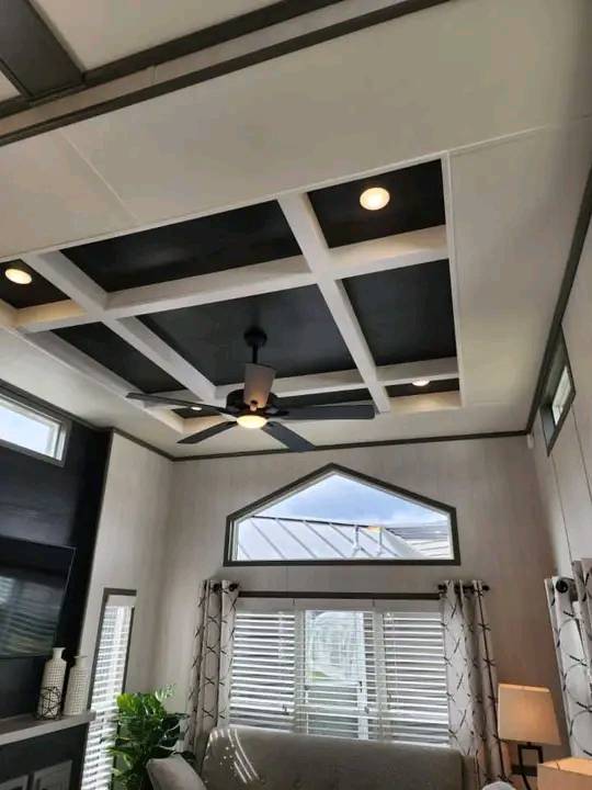 Modern living room with a coffered ceiling, ceiling fan, large windows with striped curtains, and ample natural light, creating an airy feel.