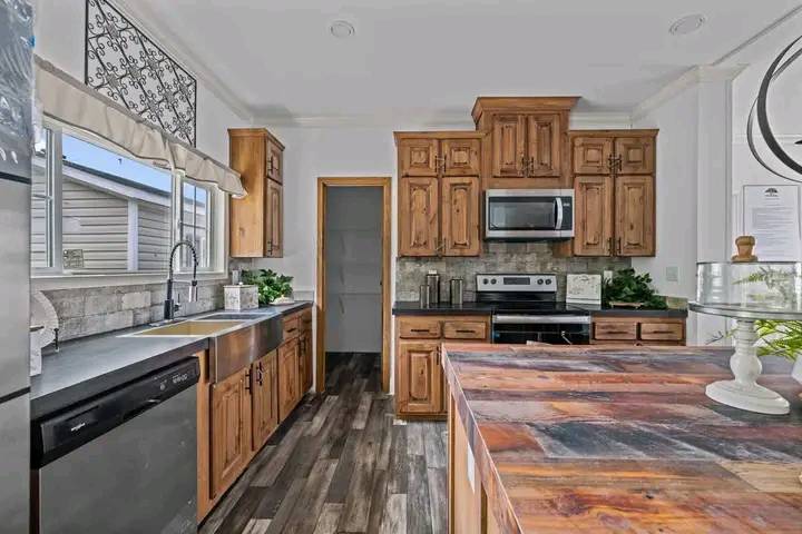 Rustic kitchen with wooden cabinets, stainless steel appliances, and a farmhouse sink. Warm tones, clay tile backsplash, and greenery add charm.