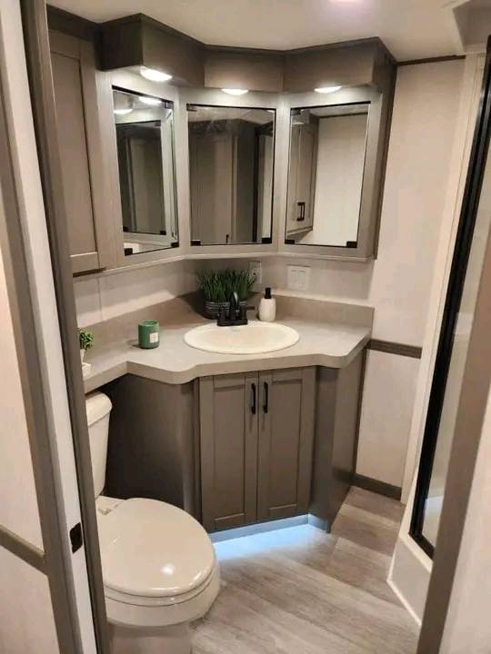 A modern bathroom features a corner sink with a gray vanity, mirrored cabinets, and wood flooring. Soft lighting creates a clean, cozy feel.