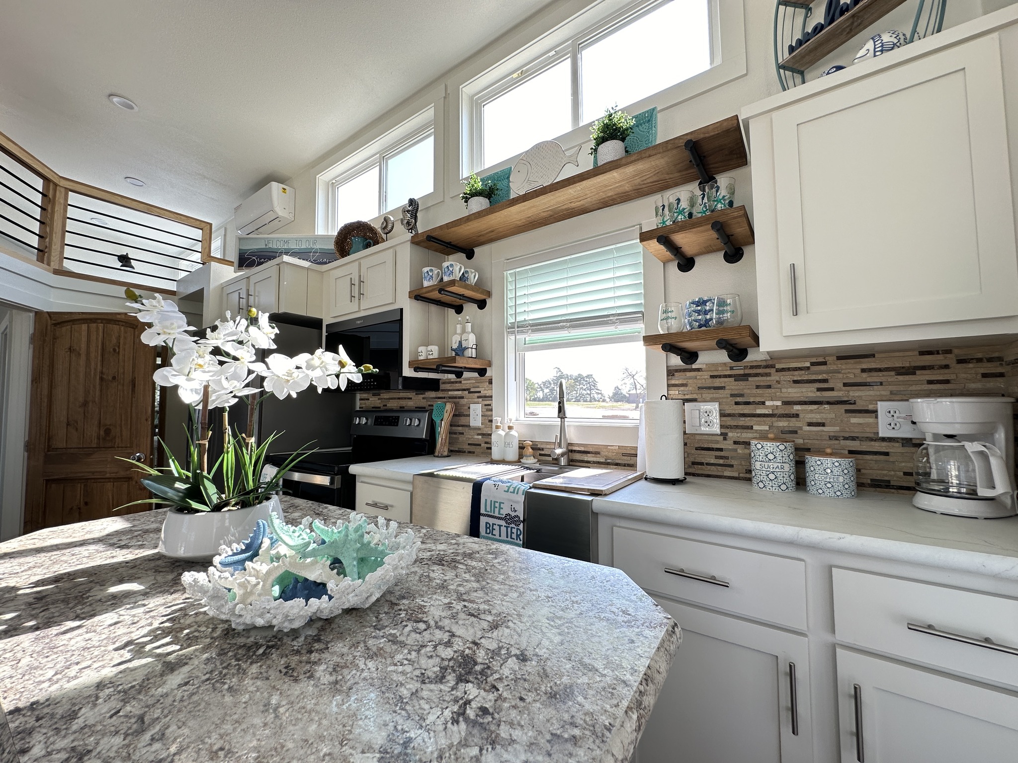 Bright, modern kitchen with white cabinets and marble countertops. Decorative white orchids and sea-themed accents add a calming coastal feel.