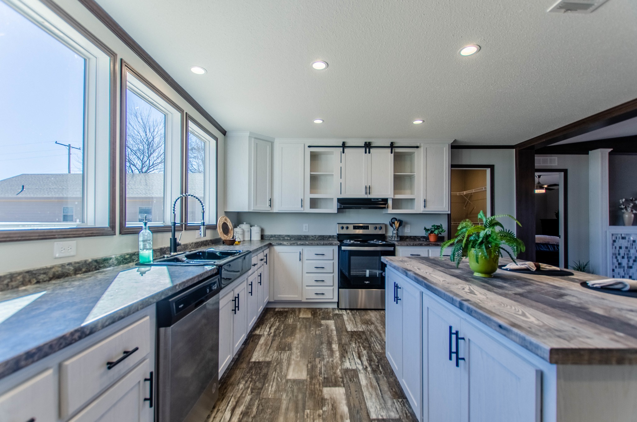 Bright modern kitchen with white cabinets, dark countertops, and a wooden island. Sunlit windows illuminate the space, creating an inviting and fresh atmosphere.