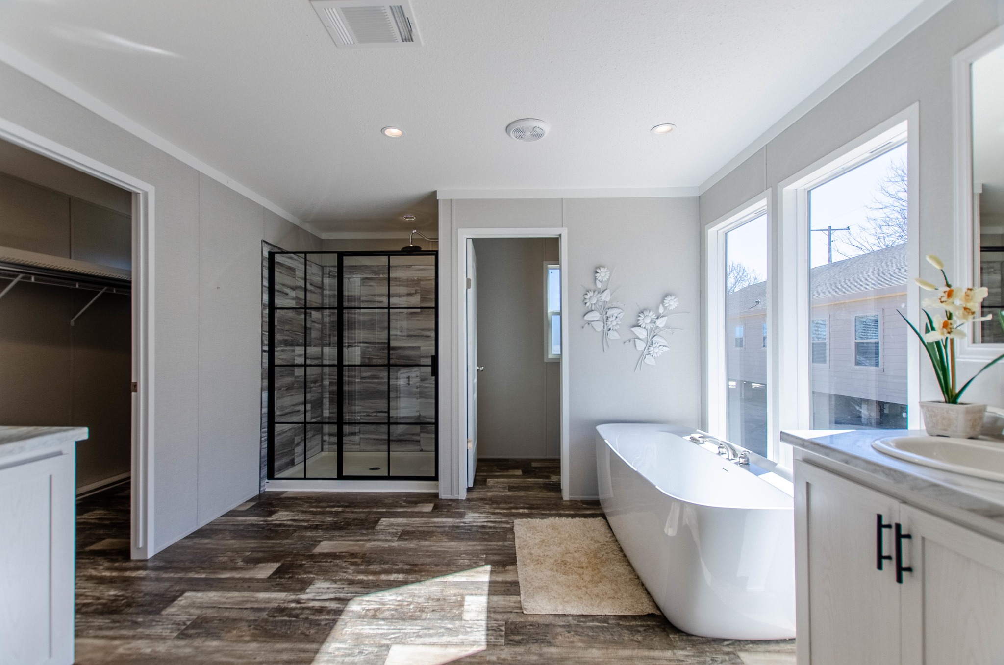 Modern bathroom with a freestanding tub, large windows, and wooden flooring. A glass walk-in shower and decorative wall art create a serene ambiance.