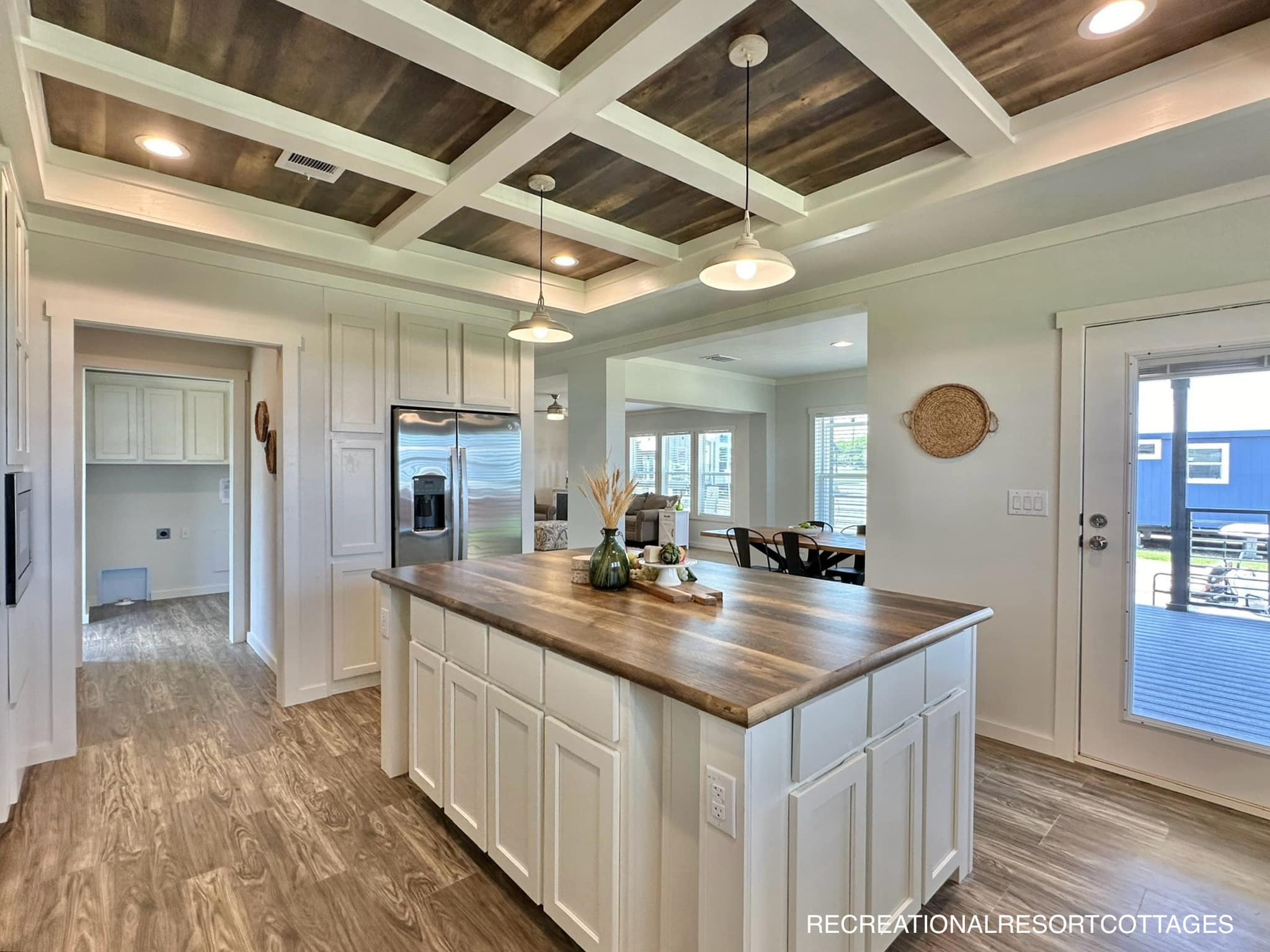 Spacious kitchen with a wooden coffered ceiling, white cabinetry, and a central island with wood countertop. Bright, modern, and inviting atmosphere.