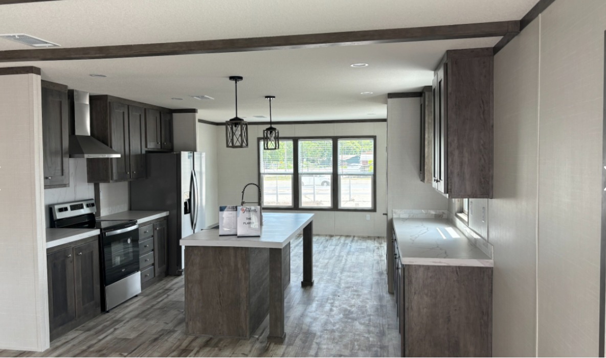 Modern kitchen with dark wood cabinets, stainless steel appliances, and an island. Large windows bring in natural light. Neutral, bright ambiance.