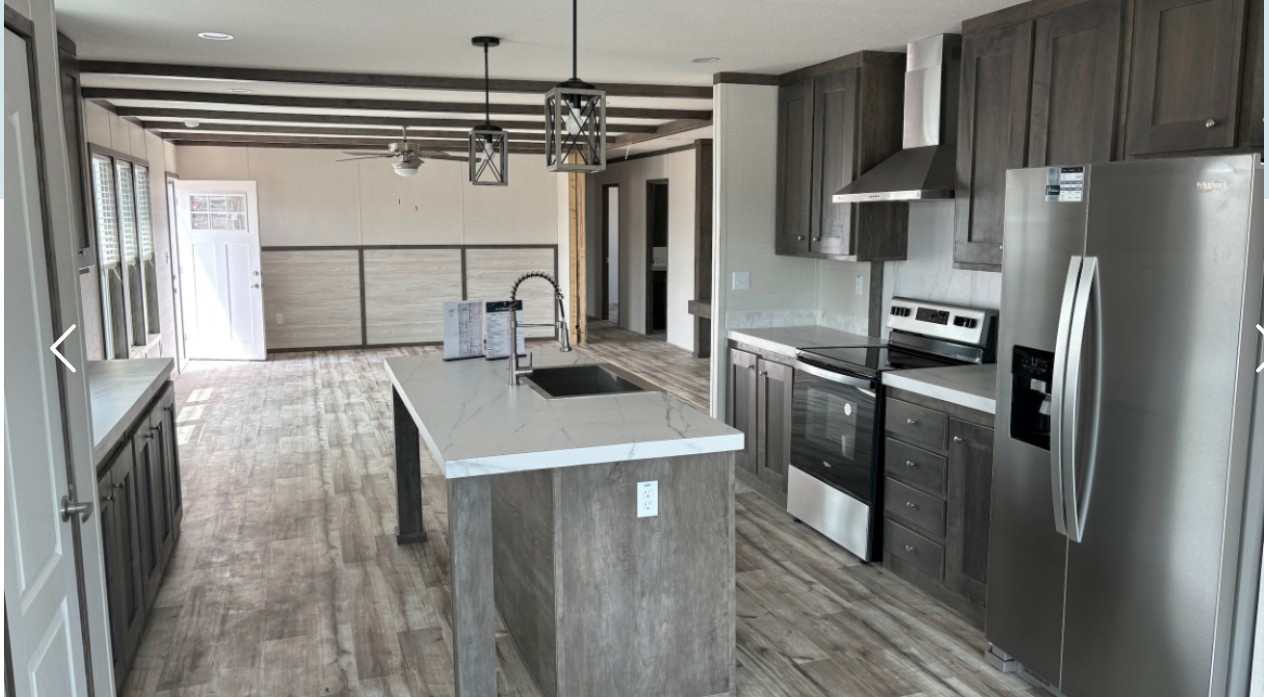 Spacious modern kitchen with gray cabinets, stainless steel appliances, and a white marble island. Bright natural light from large windows and a glass door.