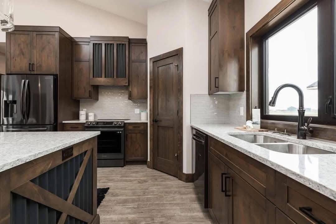 Modern kitchen with dark wood cabinets, white granite countertops, and stainless steel appliances. A large window provides natural light. Cozy and welcoming ambiance.