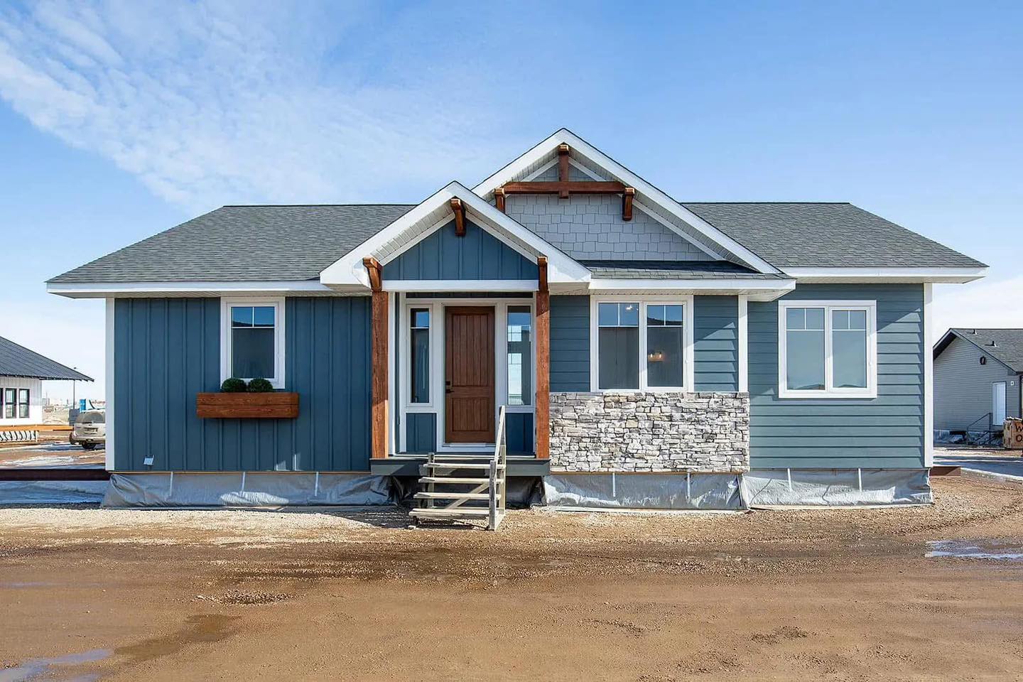 A blue, single-story house with a gabled roof, wooden beams, and stone veneer accents. Large windows and a wooden front door create a welcoming feel.