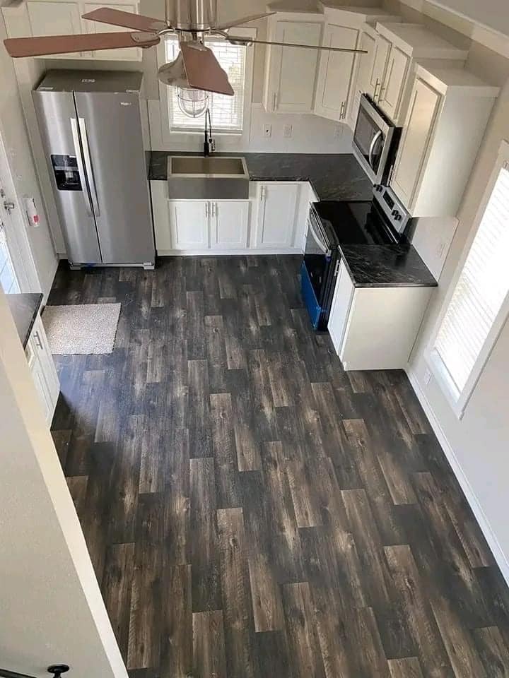 Modern kitchen with dark wooden floors, white cabinets, stainless steel appliances, and black countertops. Overhead view shows tidy ambiance.