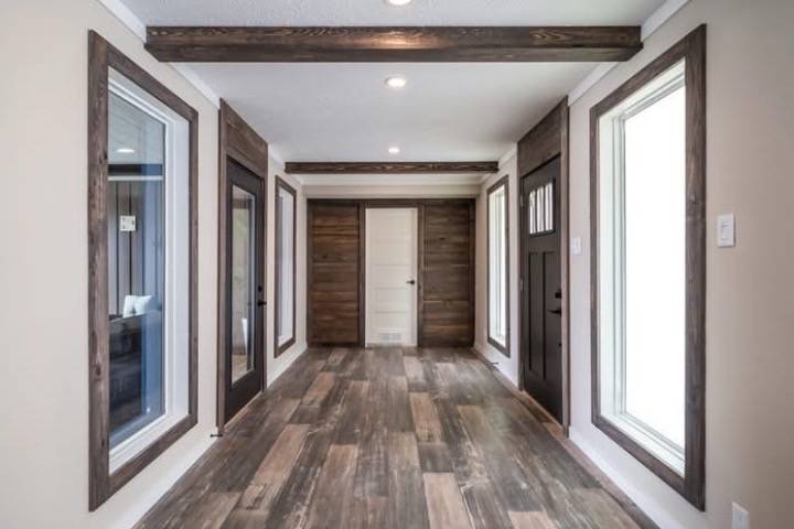 Modern hallway featuring wood-paneled walls, large windows, and a tiled floor with a rustic finish. Dark wooden ceiling beams enhance a cozy ambiance.