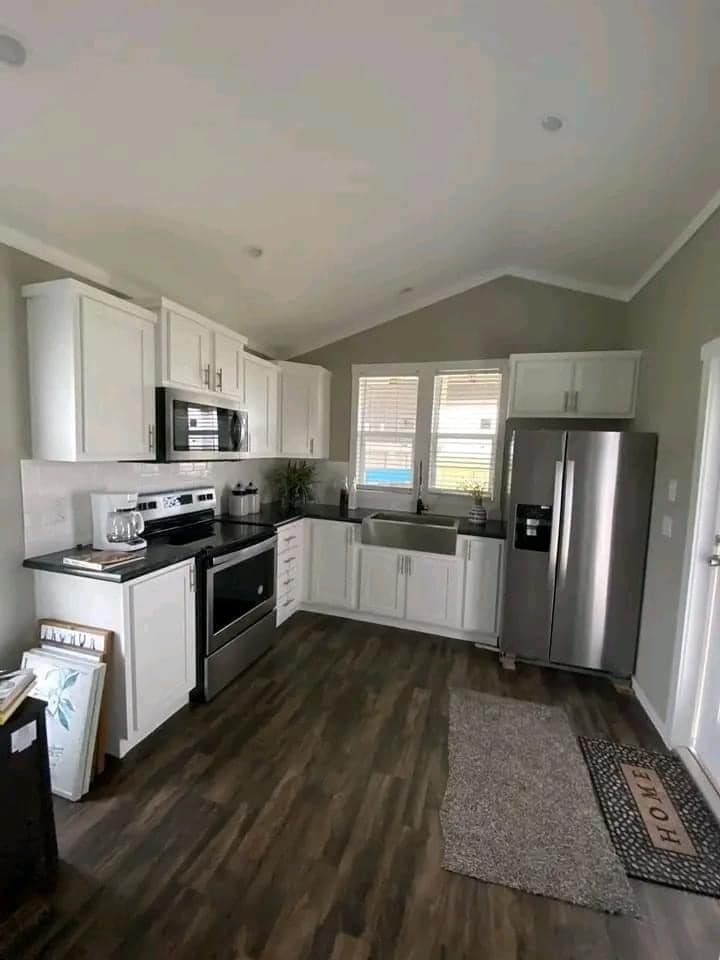Modern kitchen with white cabinets, stainless steel appliances, and dark countertops. Large windows provide natural light. Cozy and inviting atmosphere.
