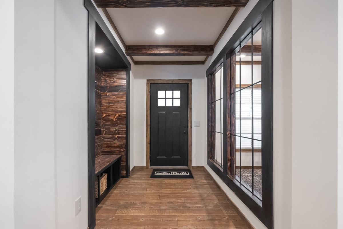 Wood-paneled hallway with a black front door, large grid windows to the right, and a built-in bench with storage to the left; a warm, inviting tone.