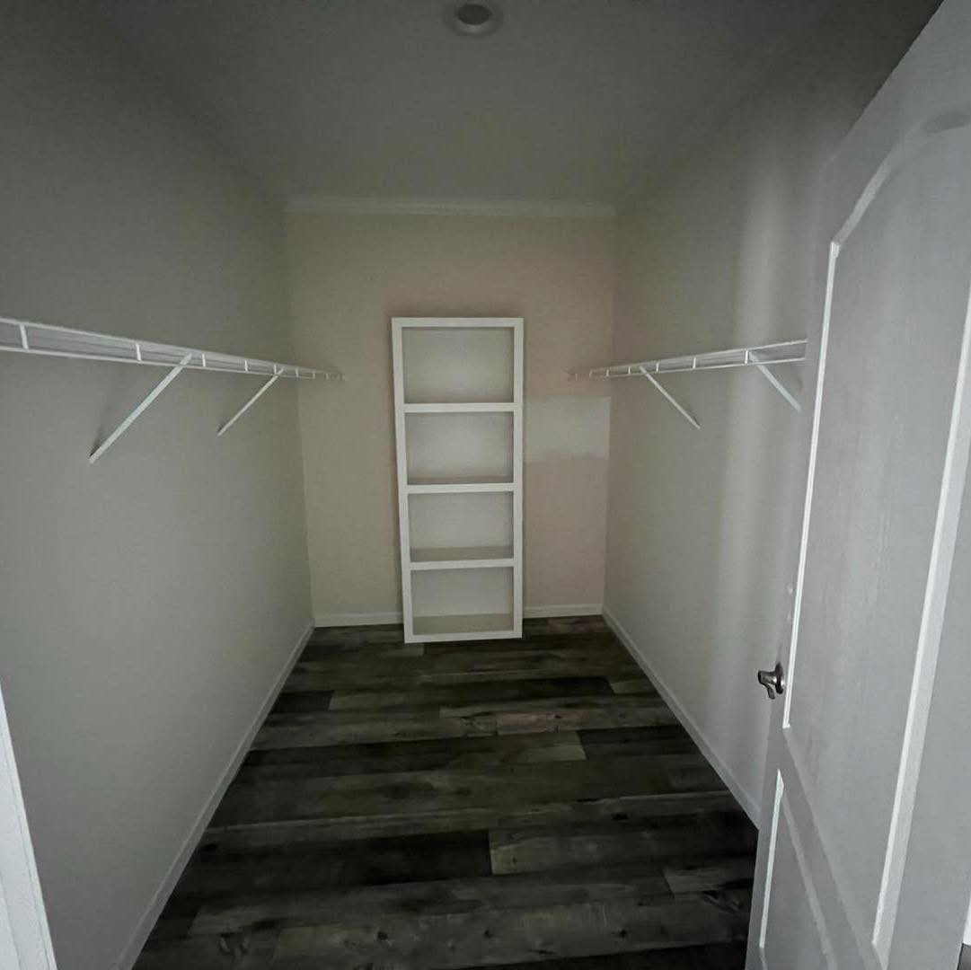 Empty walk-in closet with wooden floors and white walls. It features white metal racks on both sides and a white shelving unit at the end.