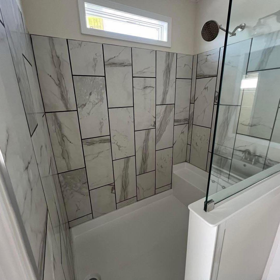 Modern bathroom with large white tiles featuring dark, asymmetrical lines. A glass divider separates the shower area, creating a clean, sleek look.
