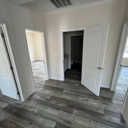 Minimalist room with three open doors revealing gray wood floors and white walls. Soft natural light enters, highlighting the calm, spacious ambiance.