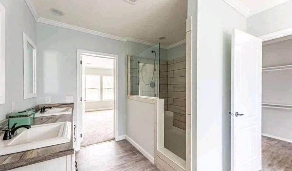 A modern bathroom features dual sinks with black faucets, a walk-in shower with gray tiles, and open doors leading to a bright adjoining room.
