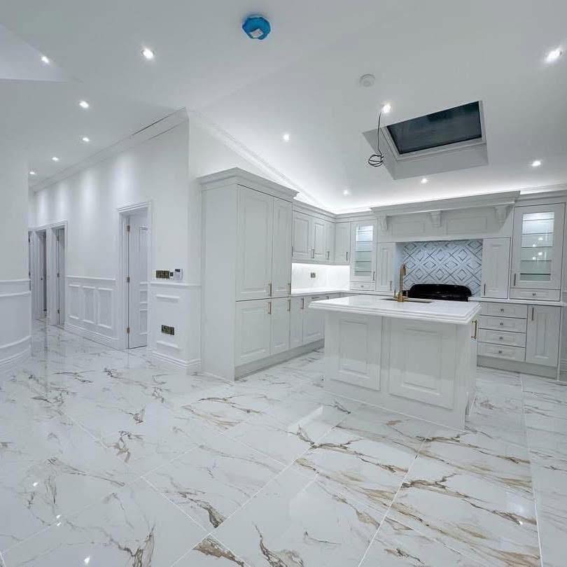 Spacious, modern kitchen with glossy white cabinets, marble flooring, and a large island. Bright lighting and elegant design create a sleek, luxurious feel.