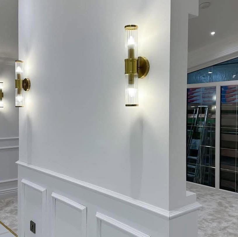Elegant hallway with modern brass and glass wall sconces casting soft, warm light. White walls and paneling create a clean, sophisticated ambiance.