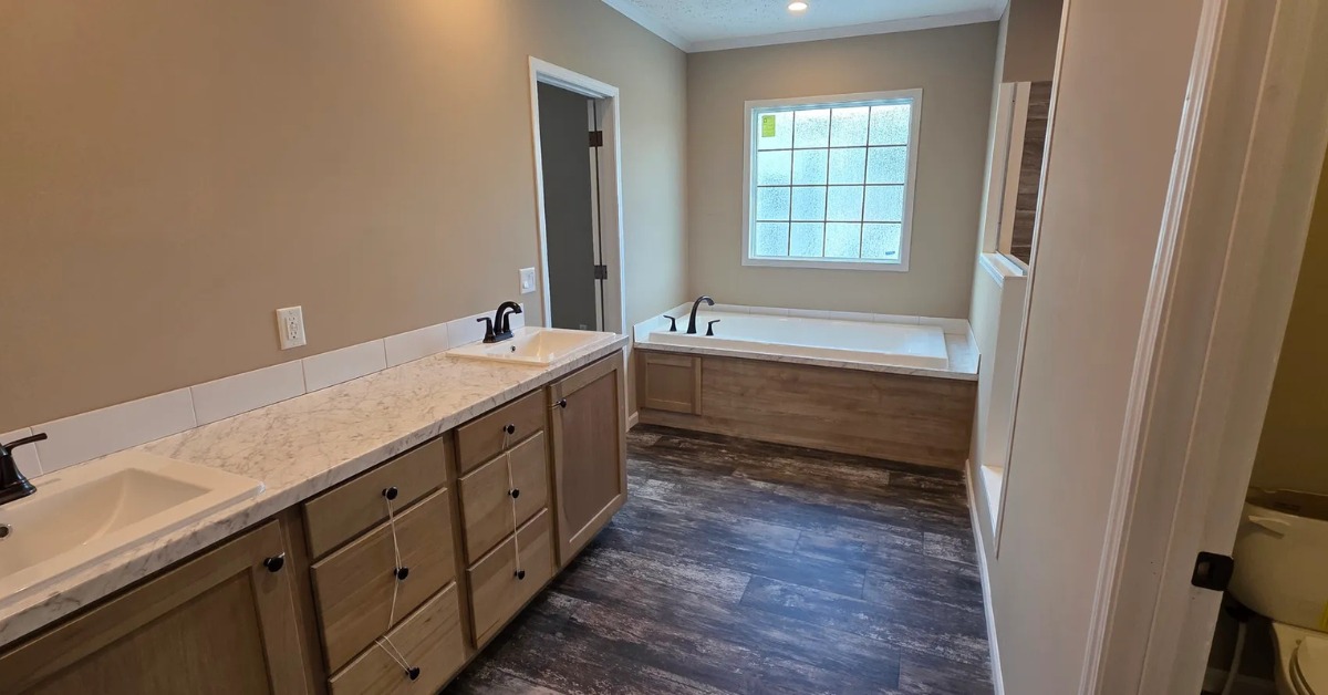 Modern bathroom with dual sinks on wooden vanity, marble countertops, and sleek black faucets. Spacious tub under a large window; warm, neutral tones.