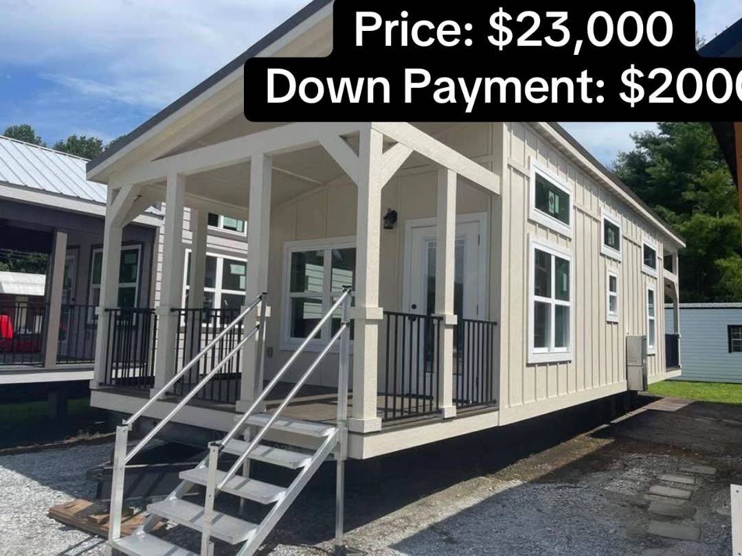 Modern tiny house with a front porch, white siding, and black railing. Text indicates a price of $23,000 and a $2,000 down payment.