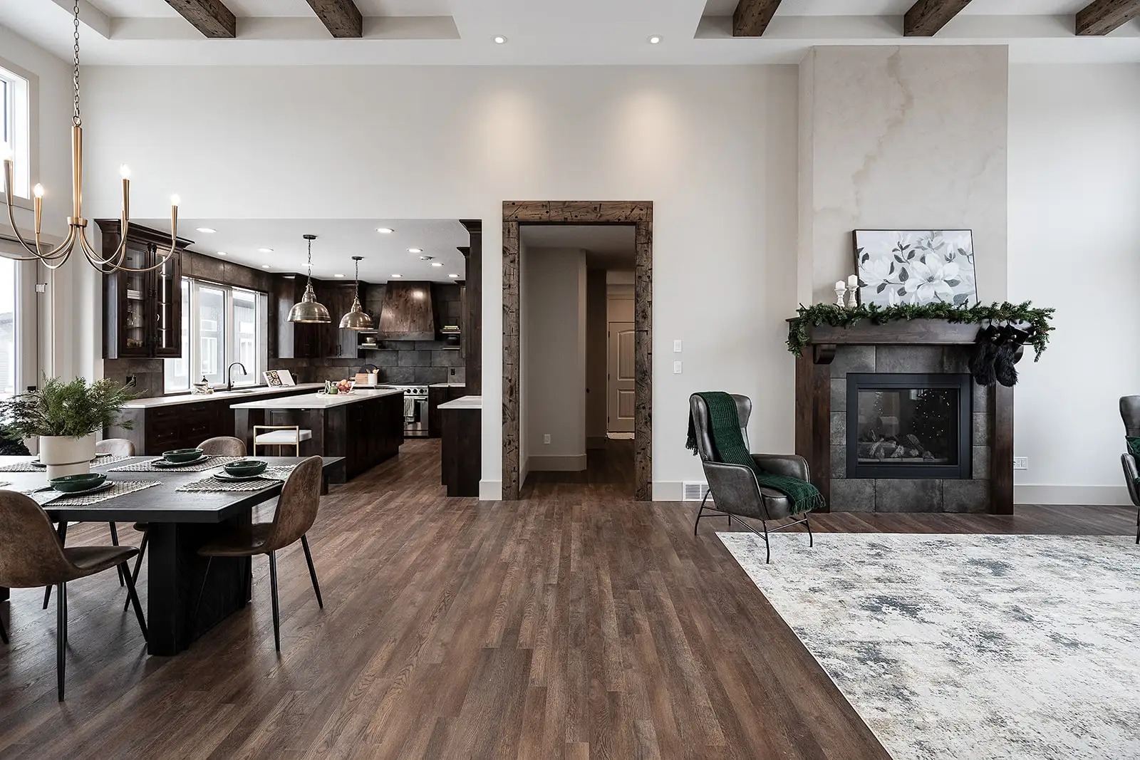 Modern open-concept living space with a dining area, dark wooden kitchen, and cozy fireplace. Hardwood floors and a soft rug add warmth and elegance.