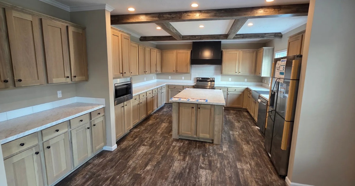 Spacious kitchen with wooden cabinets, a central island, stainless steel appliances, and dark wood floor. Exposed ceiling beams provide a rustic touch.